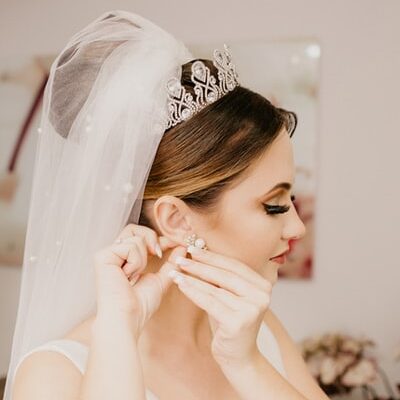 Noiva maquiada e com véu branco colocando o brinco